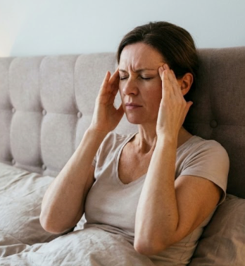 Mujer con dolor de cabeza tensional y migraña matutina masajeando sus sienes en la cama.