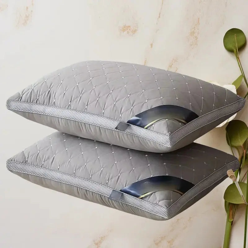 Almohadas grises de diseño acolchado apiladas sobre fondo beige, ambientadas con planta decorativa, resaltando el estilo y la calidad indeformable
