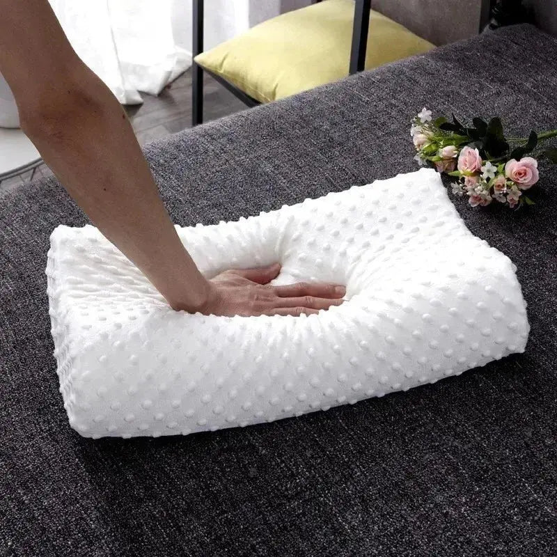 Primer plano de una mano presionando una almohada de memory foam blanca con textura de micro-puntos en relieve para demostrar su suavidad y capacidad de rebote lento sobre una cama oscura.